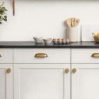 Vaaleat keittiökaapit tyylikkäillä messinkisillä nupeilla ja vetimillä.