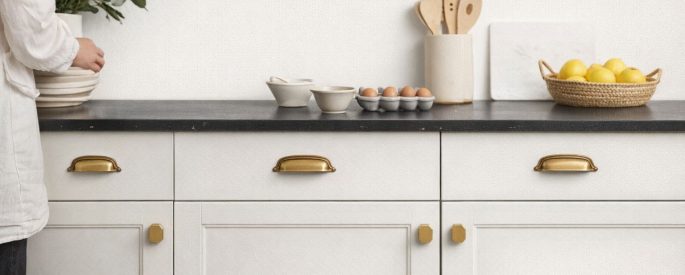 Vaaleat keittiökaapit tyylikkäillä messinkisillä nupeilla ja vetimillä.